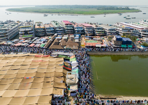 Aerial view of a multitude of people congregating near the riverbank, with boats docked and tents spread out, creating a vibrant tapestry of human activity, Charmonai, Barisal Division, Bangladesh.