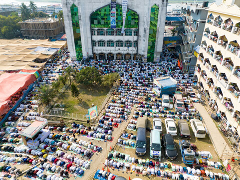 Aerial view of a large gathering of people in prayer outside a grand mosque with intricate white architecture, Charmonai, Bangladesh.