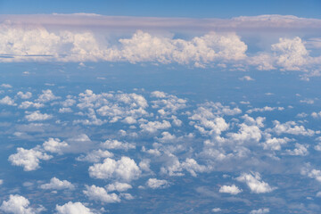 Top view of a layer of white clouds and blue sky during a passenger flight in summer season.
