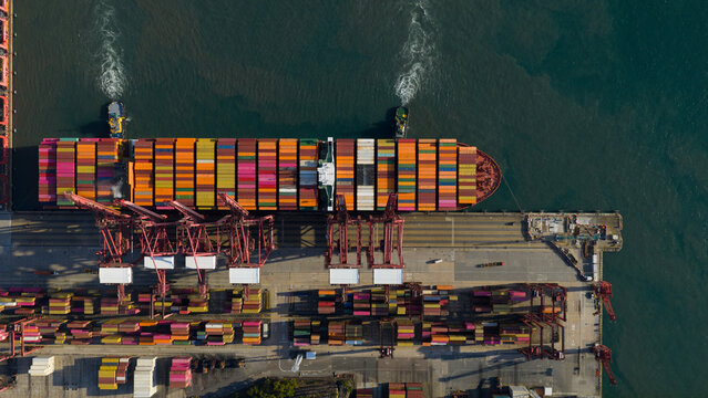 Aerial view of a colossal container ship, a floating mosaic of vibrant hues, docked amidst the industrial ballet of cranes, Shenzhen, China.