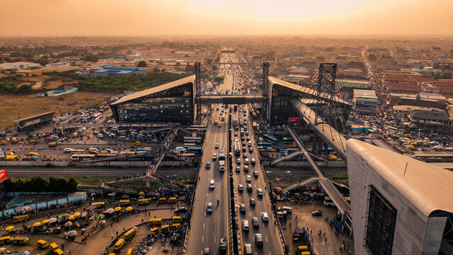 Lagos, Nigeria - 24 February 2026: Aerial view of the bustling Oshodi pedestrian overpass, a web of roads, vehicles, and buildings under a golden sky.