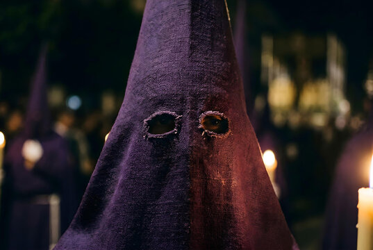 Close-up of traditional capirote hood worn during Spanish Semana Santa Holy night procession, textured fabric and eye openings visible, candlelight reflecting on surface