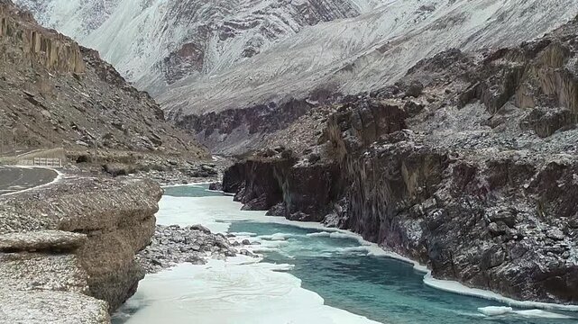 Half-frozen river flowing beside a mountain road in winter in Ladakh, India, with ice covering part of the water while the remaining stream continues to flow through the cold Himalayan landscape.
