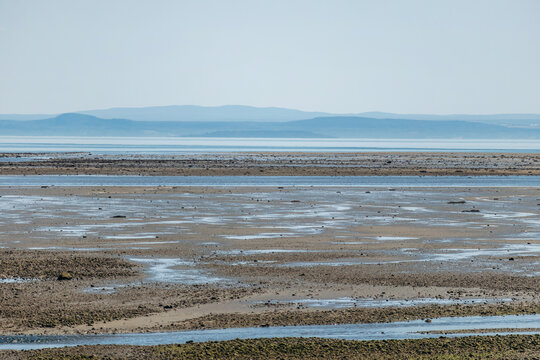 Low tide landscape with exposed tidal flats, shallow water pools and distant coastline along the Saint Lawrence River in La Malbaie, Quebec