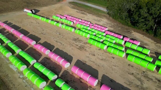 Truck positioned near rows of wrapped cotton bales awaiting transport on farmland near Headland, Henry County, Alabama, United States during cotton harvest season, aerial drone static view.