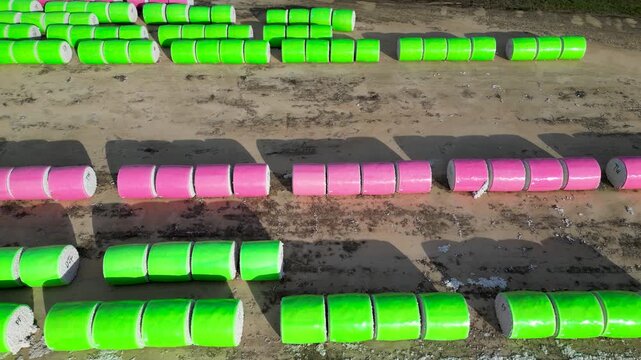 Parallel rows of green and pink wrapped cotton bales stored on farmland near Headland, Henry County, Alabama, United States during harvest season, slow panning drone shot.