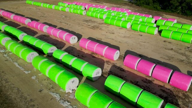 Close aerial view of green and pink plastic wrapped cotton bales aligned on farmland near Headland, Henry County, Alabama, United States during autumn harvest operations.
