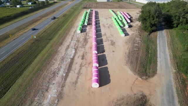 Wrapped cotton bales arranged in long rows beside a rural road near Headland, Henry County, Alabama, United States during autumn harvest logistics operations, aerial view.