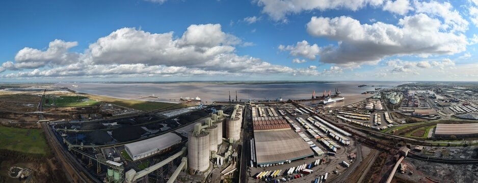 Immingham, United Kingdom - 15 March 2026: Aerial view of docks where ships rest near a network of roads, warehouses, and open storage, under a vast sky filled with fluffy clouds.