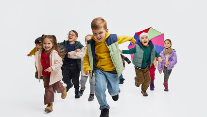 Obraz premium Children running together wearing bright kids outfits in white studio. Concept of playful childhood lifestyle, colorful seasonal clothing and energetic kids fashion campaign.
