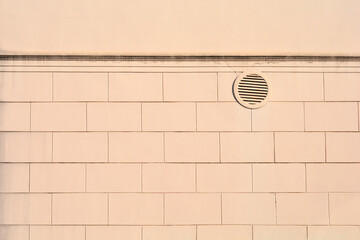 A light beige building facade featuring a circular ventilation grille and a structured pattern of rectangular blocks under a horizontal cornice line © nahhan