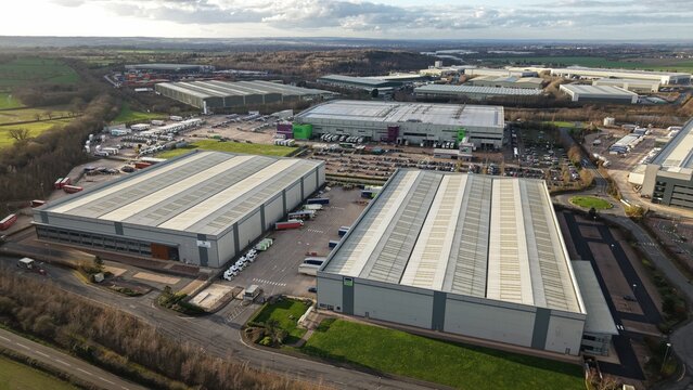 Tamworth, United Kingdom - 21 February 2026: Aerial view of the DRAXLMAIER distribution centre, its vast rooftops mirroring the pale sky, while rows of parked vehicles form a colorful mosaic below.