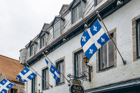 Quebec City, Canada - August 23, 2025: Quebec provincial flag with fleur de lis symbols hanging on facade of historic building in Place Royale area