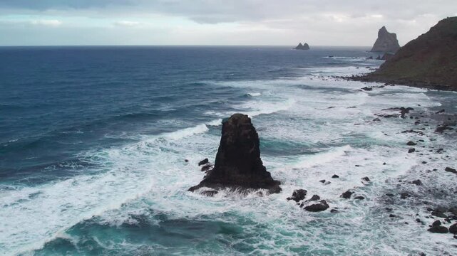 Dramatic aerial perspective of the rugged coastline at Benijo beach, featuring the iconic Roque de la Rapadura and powerful ocean waves. Tenerife, Canary Islands