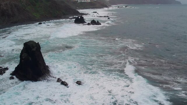 Dramatic aerial perspective of the Atlantic Ocean with powerful waves and white foam breaking against the Roque de la Rapadura in Anaga. Tenerife, Canary Islands