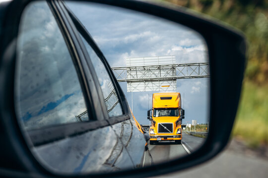 Montreal, Canada - August 24, 2025: Yellow semi truck visible in car side mirror while driving on highway near Montreal