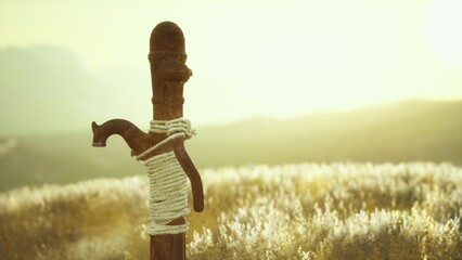 A wooden post tied with rope stands tall amidst lush grass, glowing under the golden sunset. The serene atmosphere captures a moment of quiet beauty in the countryside. © icetray