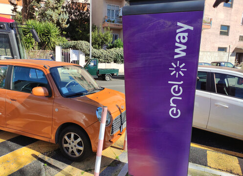 Rome, Italy - February 27, 2026: Orange compact car parked next to a purple electric vehicle charging station with visible branding in an urban street setting