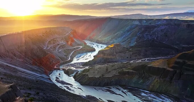 Aerial view of spectacular sunrise over Anjihai Grand Canyon with red sedimentary layers and a winding road in Xinjiang, China. Eroded geological landscape.