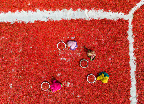 Aerial view of vibrant red chilies spread out to dry under the sun, punctuated by the presence of workers and circular objects, Sariakandi, Rajshahi Division, Bangladesh.