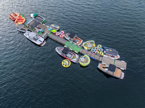 Aerial view of boats tethered together with floating platforms and colorful inflatables on the dark water's surface, Alqueirao, Braga, Portugal.