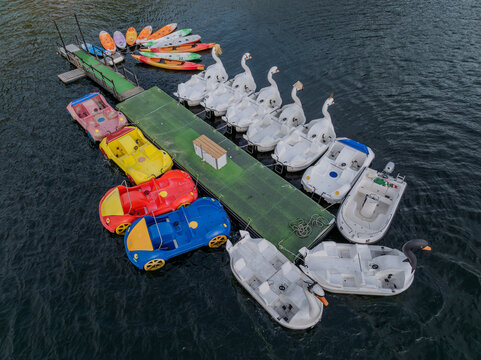 Aerial view of a vibrant collection of swan pedal boats and colorful kayaks clustered around a dock, contrasting with the deep blue water, Alqueirao, Braga, Portugal.