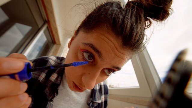 Female model crafting makeup look using smartphone camera under morning sun