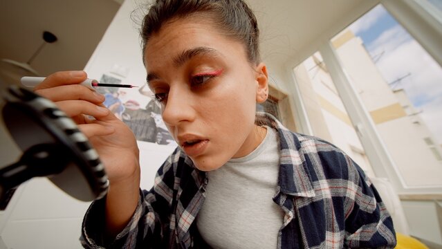 Woman meticulously applies subtle eyeliner with calm focus in daylight