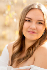 Naklejka premium Close-up portrait of a young woman with flowing brown hair and a gentle expression, bathed in warm, diffused sunlight filtering through foliage