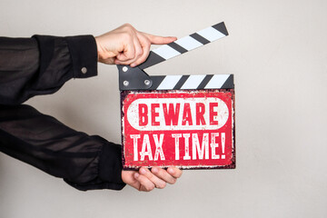 Obraz premium Beware Tax Time Warning Sign on Film Clapper Board Held in Hands