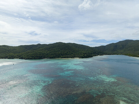 Aerial view of turquoise waters meet verdant hills under a vast sky, creating a tranquil coastal panorama, Karimunjawa, Central Java, Indonesia.