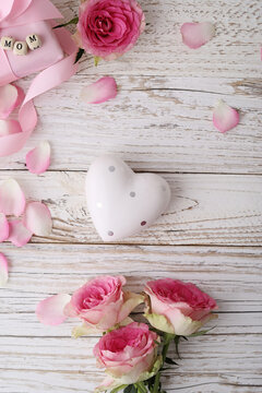 mothers day background with rose flowers, ceramic heart, pink ribbon bow and gift box