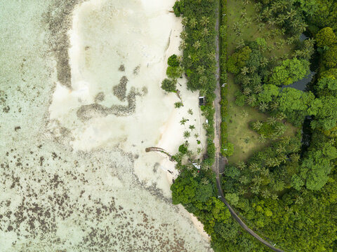 Aerial view of the turquoise waters gently caressing the pristine white sands near a lush green forest, Bobby Beach, Karimunjawa, Central Java, Indonesia.