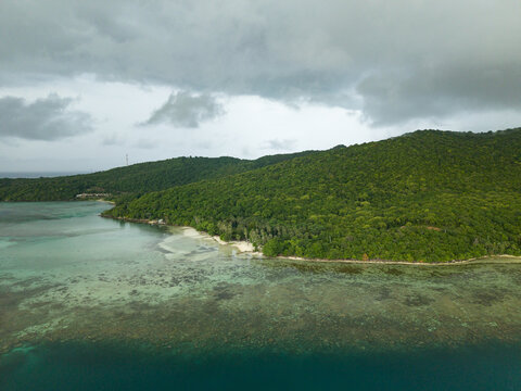 Aerial view of the lush green island meeting the turquoise sea under a dramatic sky, Karimunjawa, Central Java, Indonesia.