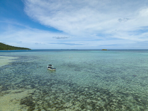 Aerial view of the turquoise waters meet the sky, a lone boat sailing gently near Bobby Beach, Karimunjawa, Central Java, Indonesia.