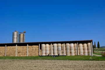 Naklejka premium Hay Bales Stored in Agricultural Barn with Silos in Tuscan Countryside, Italy