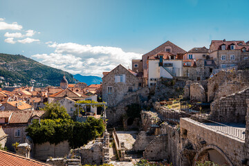 Obraz premium landscape shot of dubrovnik old town in croatia with red roof housing and detailed mediaval baroque stone architecture and bright green foliage and trees with clear blue summer skies above & mountains