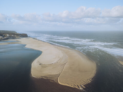 Aerial view of where the ocean meets the lagoon, the sandy shore creating a mesmerizing contrast against the deep blue waters, Lagoa de Obidos, Leiria District, Portugal.
