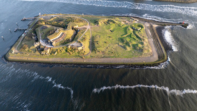 Aerial view of a small island fortification surrounded by dark waters, its green grass contrasting with the stone structures, Borkum, Germany.