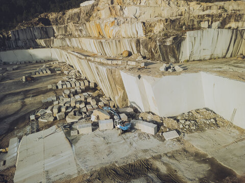 Aerial view of a vast quarry's stark white stone terraces contrasting against the earth-toned backdrop, revealing the scale of industrial extraction, Porrino, Pontevedra, Spain.