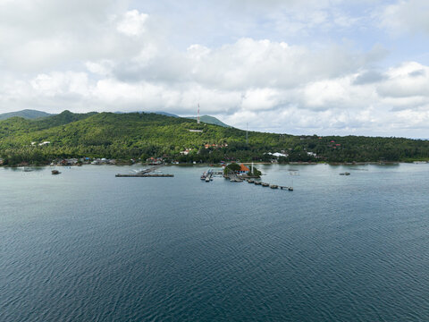 Aerial view of the Karimunjawa ferry harbour where boats bob gently on the tranquil turquoise sea against the verdant backdrop of the island, Karimunjawa, Jawa Tengah, Indonesia.