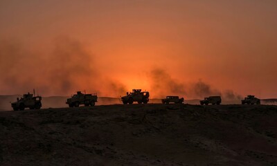 Military vehicles in silhouette at sunset with smoke
