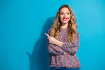 Young woman in a cozy sweater points to the left with a bright smile against a blue background...