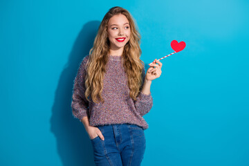 Young woman with red heart wand smiling against blue background