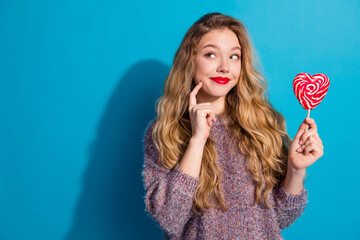 Young stylish woman with a heart shaped lollipop smiles against a blue background promoting fashion...