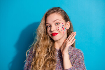 Young stylish woman with glitter makeup posing with hand on blue background wearing a cozy sweater...