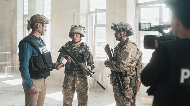 Cameraman recording video of interview soldiers. People wearing safety helmets and bulletproof vests having conversation in smoky abandoned buildings. Armed forces telling terrible stories during war.