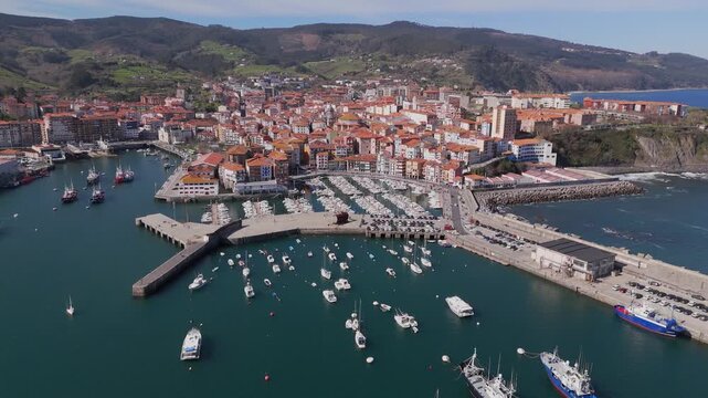 Aerial counterclockwise arc along Bermeo marina with yachts and church, Spain