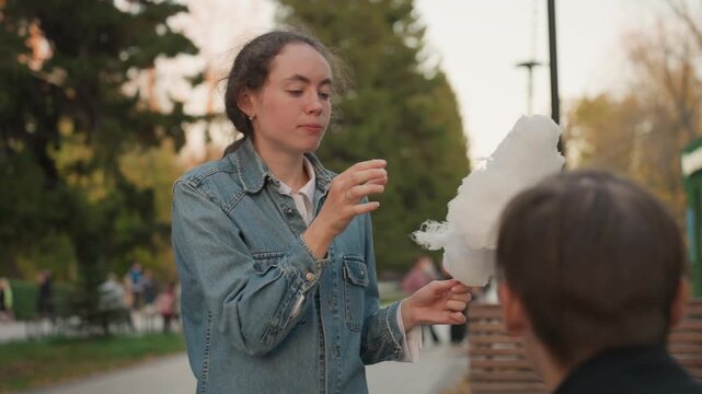 Park caucasian woman feeding cotton candy to seated relative, denim jacket, autumn trees, candid sharing moment playful taste test, tender gestures, public bench, soft evening light, authentic family