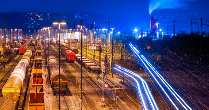 Large marshalling yard in Hagen-Vorhalle (Germany) on a cold winter night. Atmospheric panorama with artificial lighting. Countless freight cars and parked trains stand on parallel tracks.